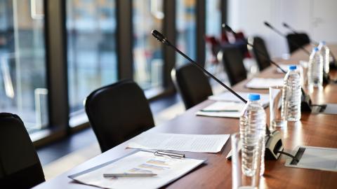A long table with several chairs behind it with microphones pointed in the direction of the chairs, where speakers would sit.