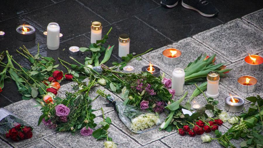 Bouquets of flowers and candles are arranged on the ground as a memorial.
