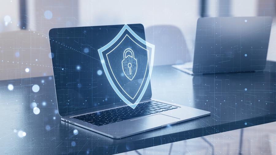 Laptop with a digital shield symbol onscreen signifies cybersecurity concept, blended with an office interior background.