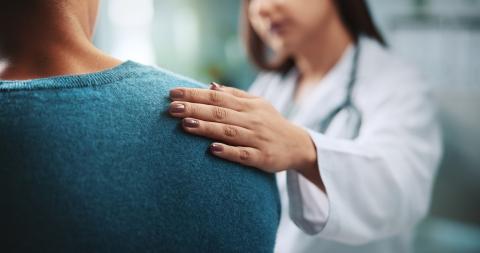 A woman wearing a white doctor's coat rests her hand on a patient's back to show support.